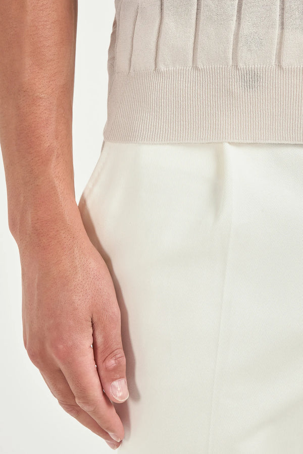 Close-up of a hand wearing a beige top and white pants with a hand on a white background