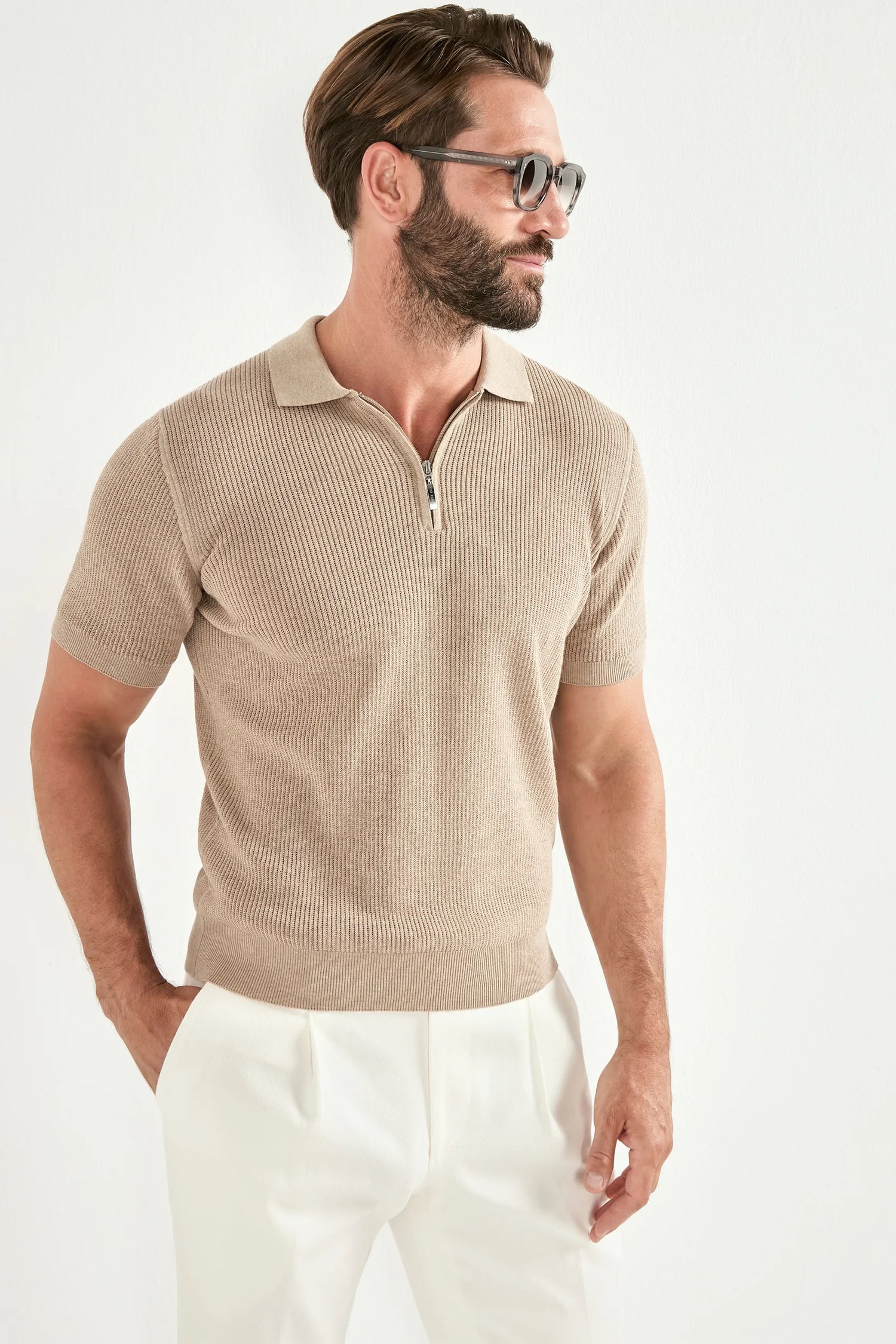 Man wearing a beige short-sleeve ribbed polo shirt and white pants on a white background