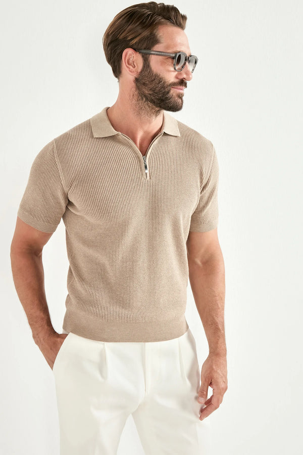 Man wearing a beige short-sleeve ribbed polo shirt and white pants on a white background