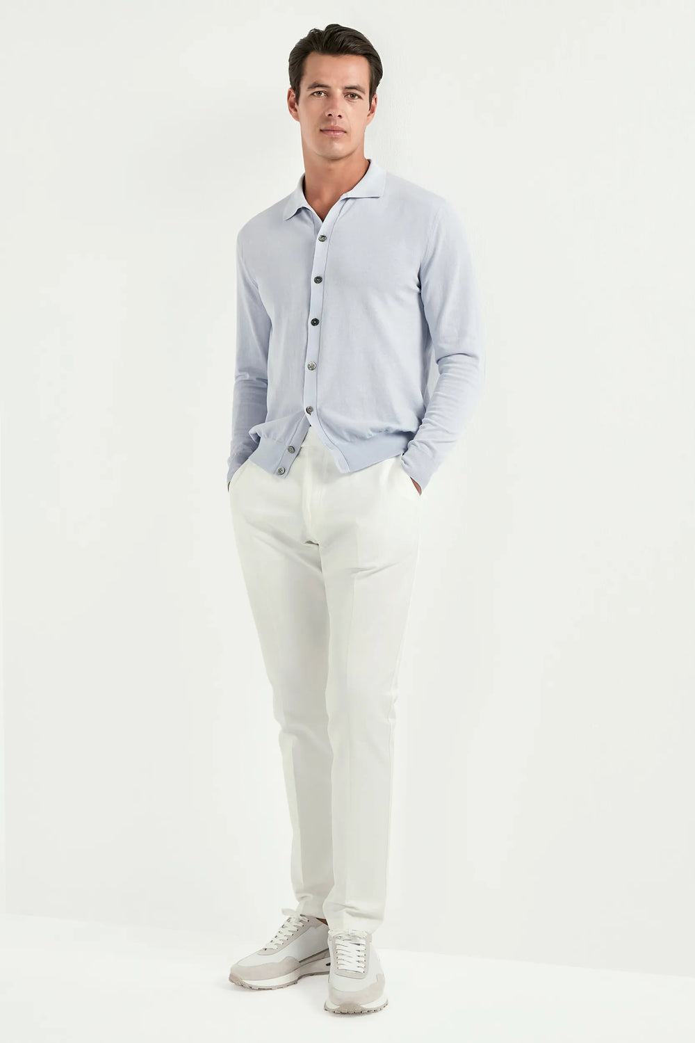 Man wearing a light blue button-up shirt, white pants, and gray shoes on a white background