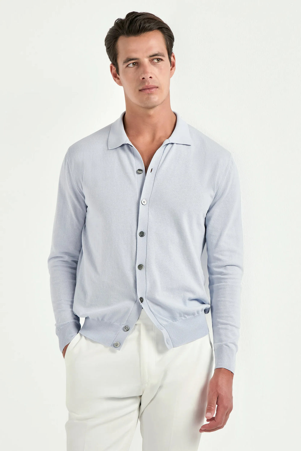 Man wearing a light blue button-up shirt and white pants on a white background