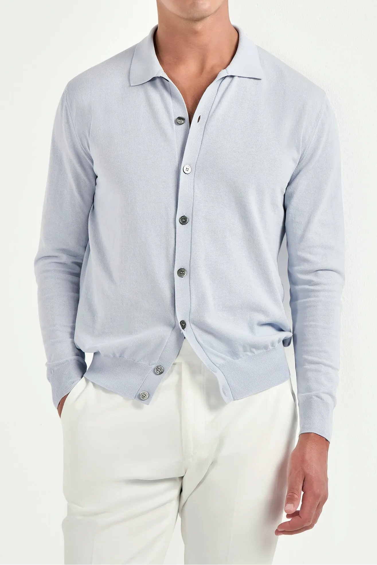 Man wearing a light blue button-up shirt and white pants on a white background