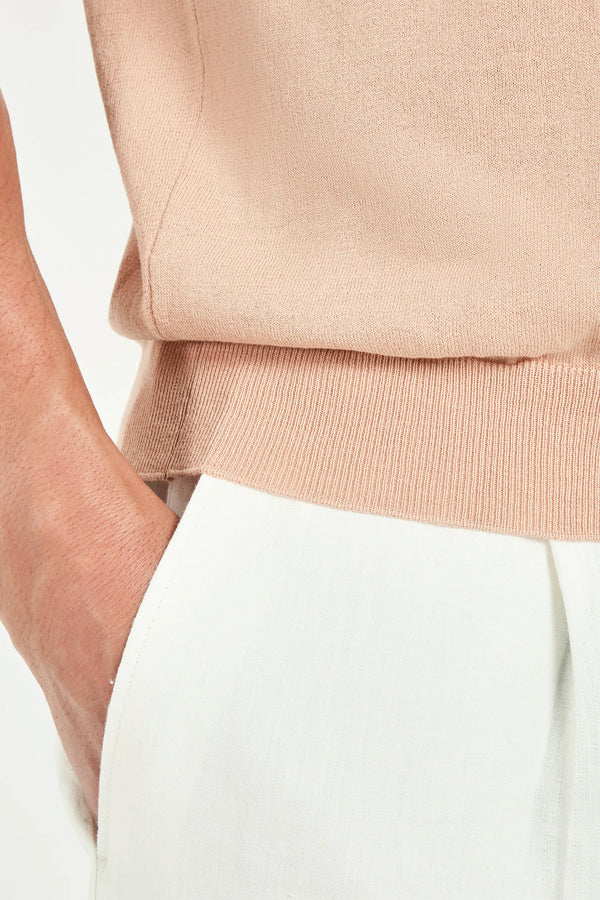 Close-up of a person wearing a beige top and white pants on a light background