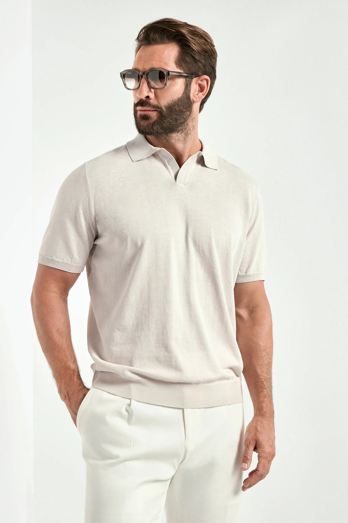 Man wearing a light-colored polo shirt and white pants on a plain background
