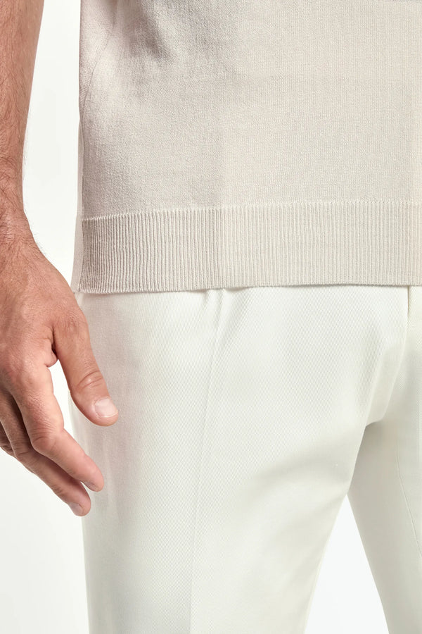 Close-up of a person wearing a light-colored sweater and pants on a plain background