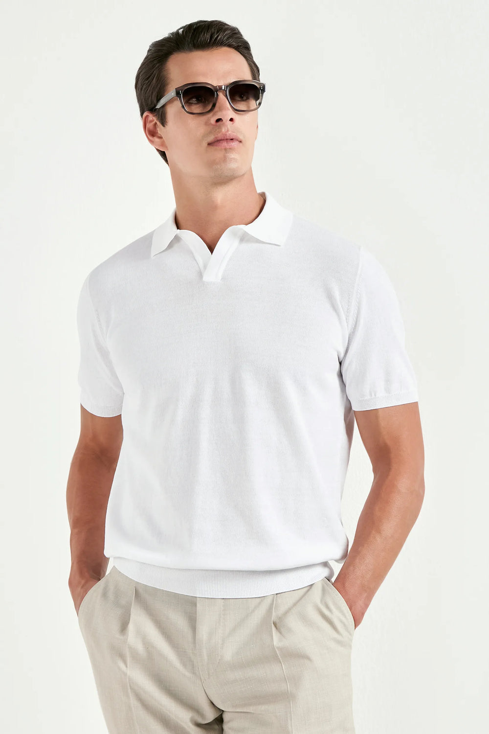 Man wearing a white polo shirt and sunglasses on a light gray background