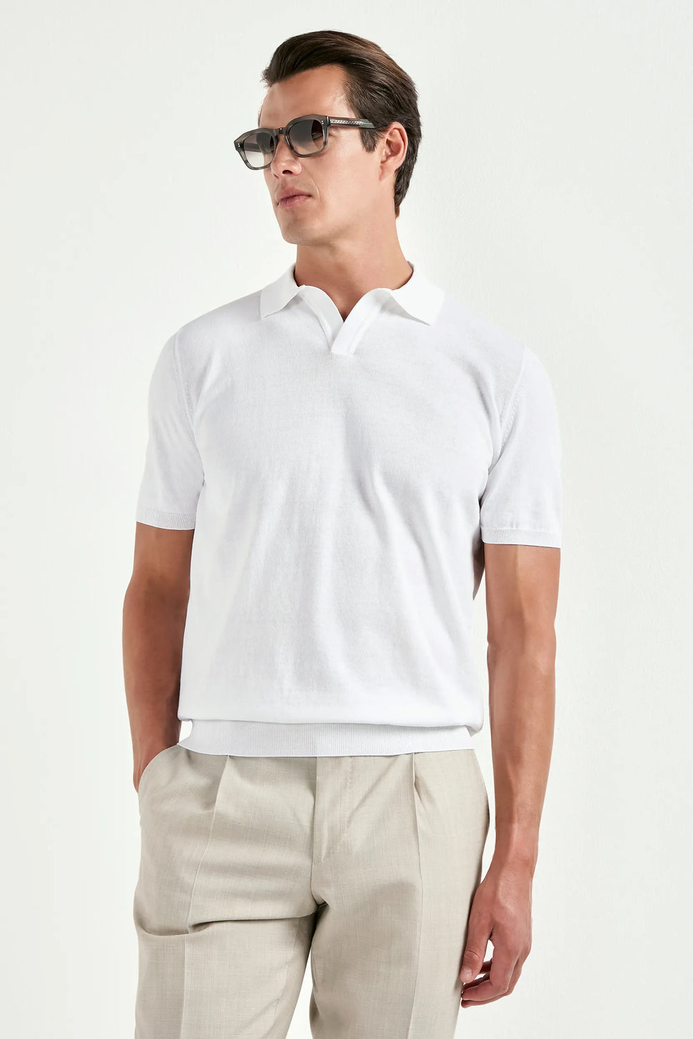 Man wearing a white polo shirt and beige pants on a white background