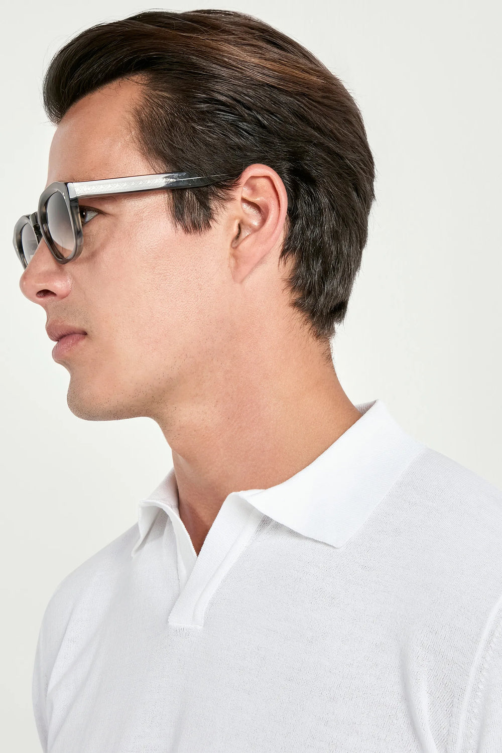 Man wearing sunglasses and a white polo shirt against a plain background